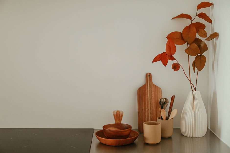 A minimalist kitchen corner with wooden bowls, a vase with autumn leaves, and cooking utensils on a countertop.