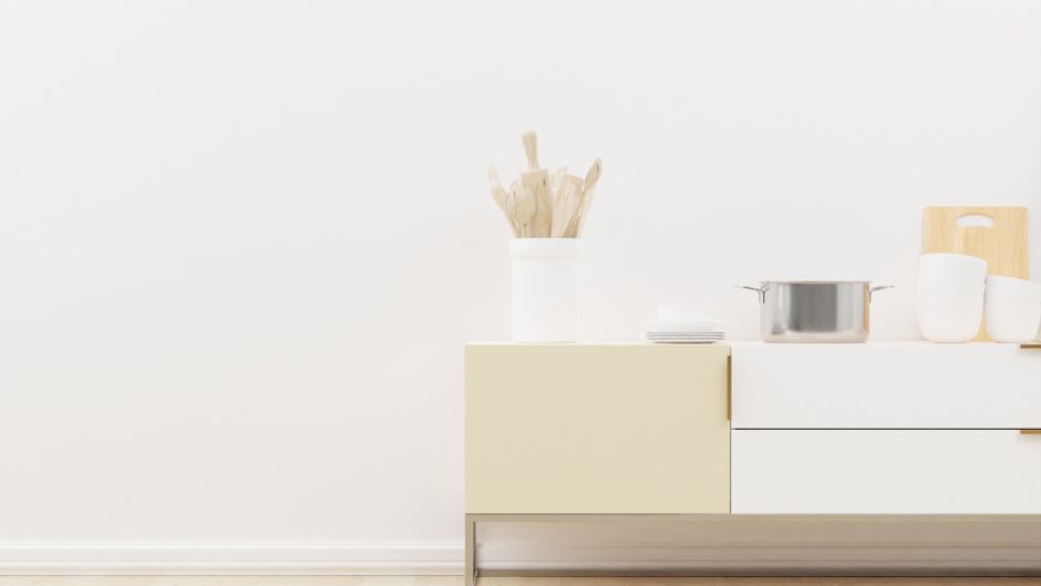 A minimalist kitchen counter setup featuring utensils, bowls, and a pot on a neutral backdrop.