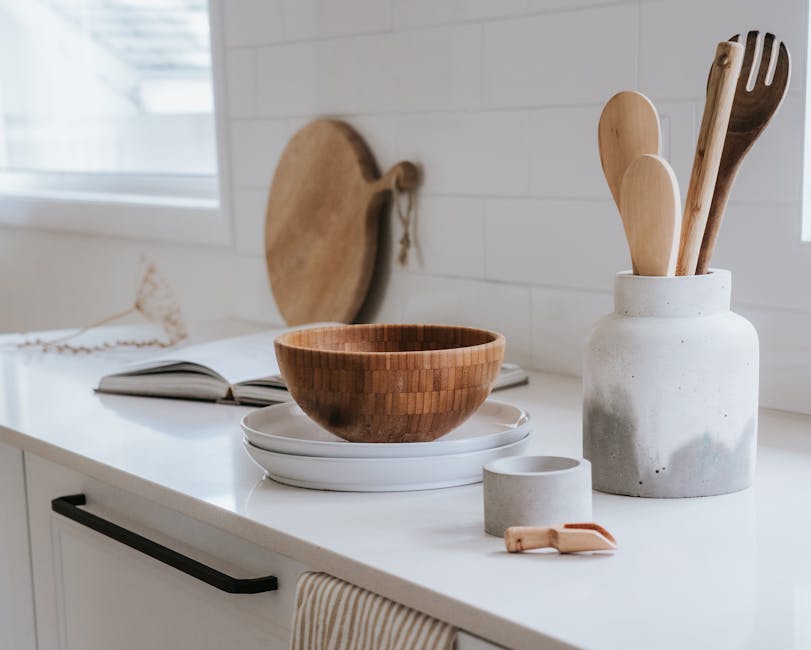 A minimalist kitchen counter with wooden utensils and a bowl in a bright setting.